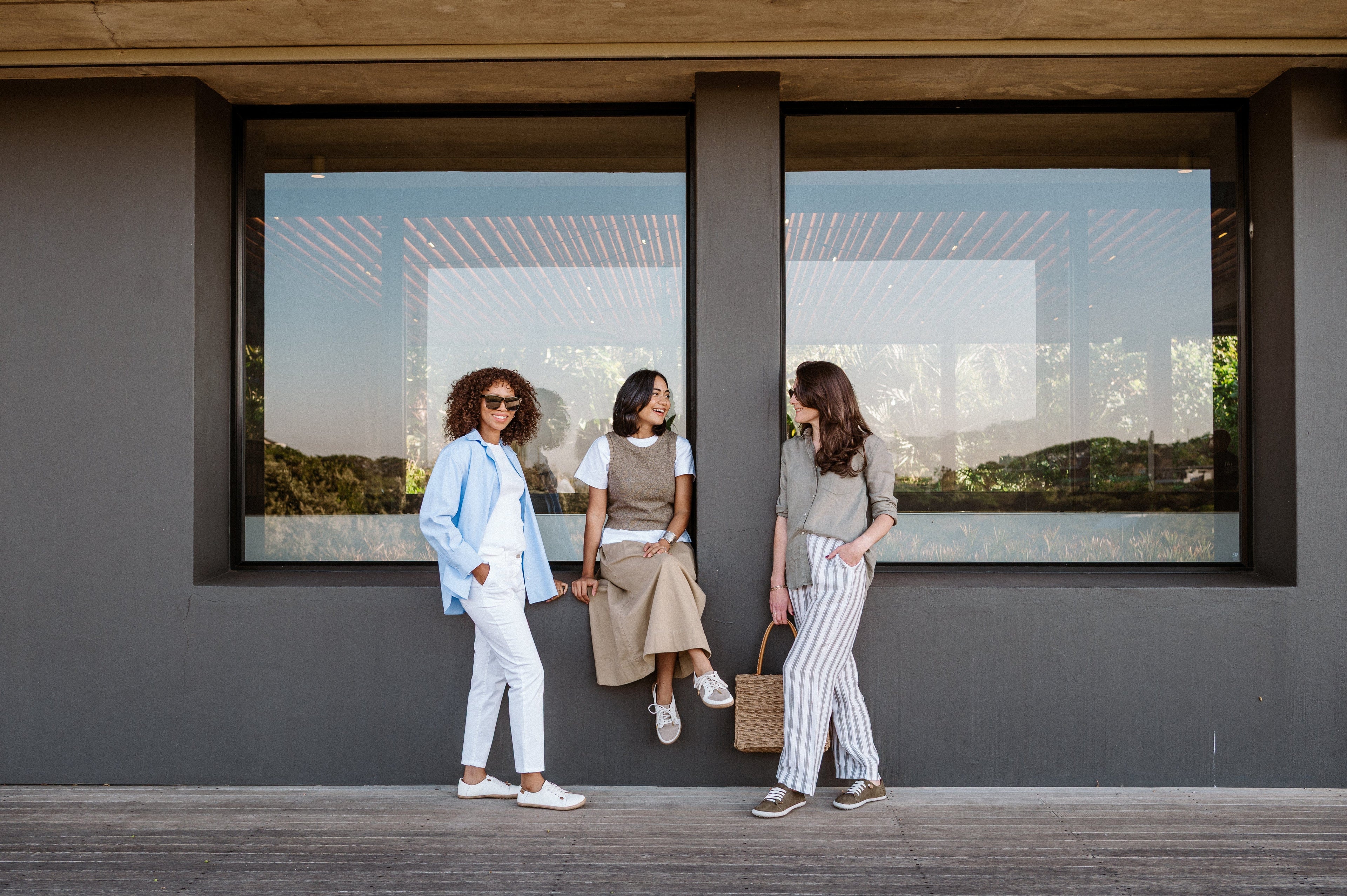 Three women standing in front of a modern building with large windows displaying a scenic view.