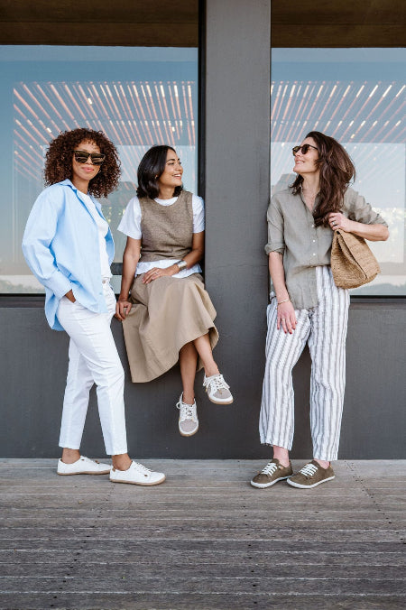 Three women posing together on a wooden deck with a modern building in the background.